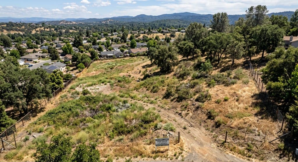 Drone photo of an overgrown, sloped vacant lot for sale next to a residential neighborhood